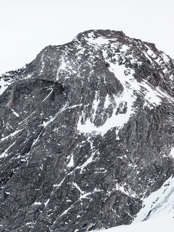 Snötäckt berg med grå himmel bakom sig i alpin miljö.